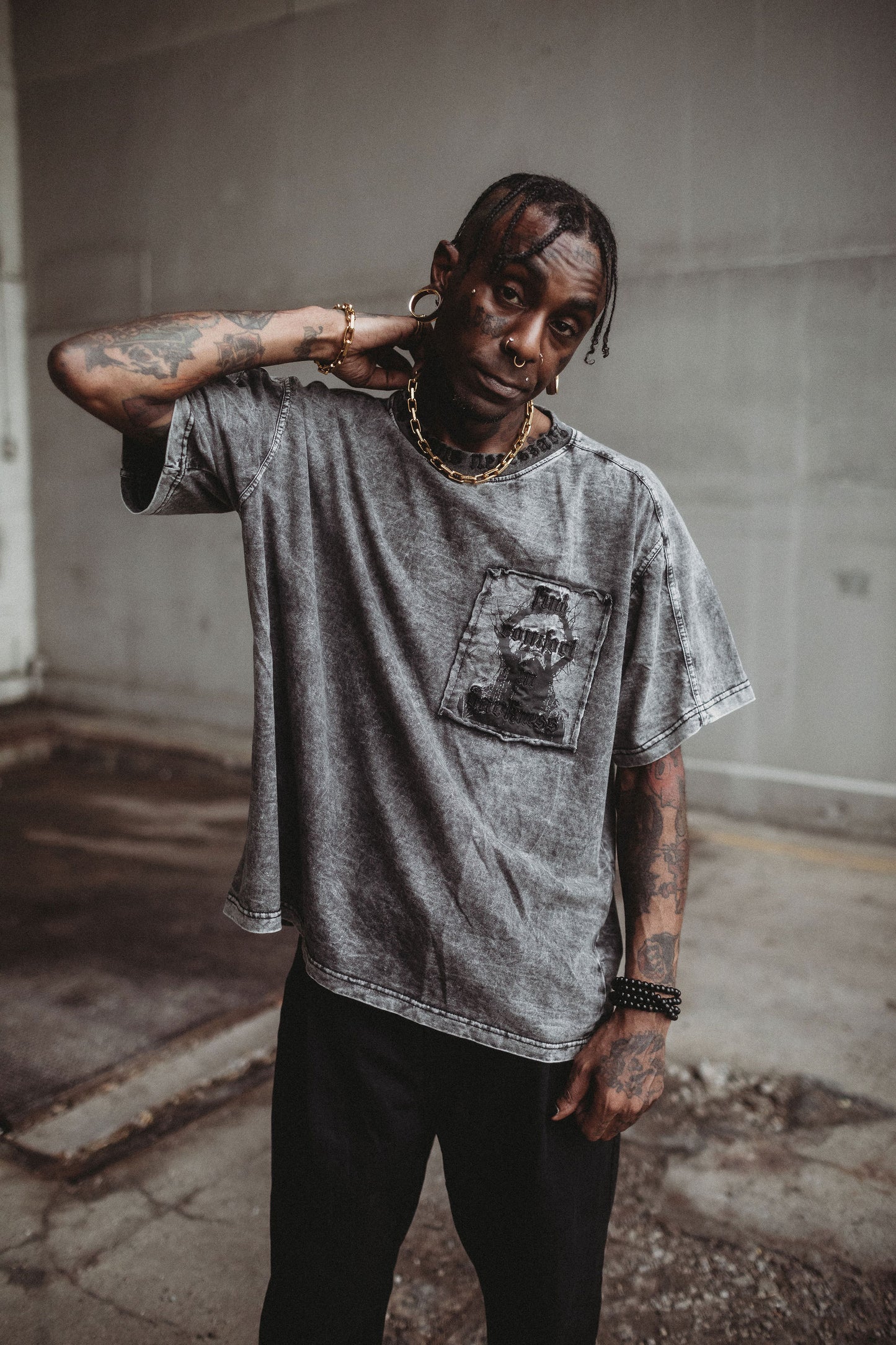 Person wearing a gray t-shirt with a graphic design, standing in an abandoned building.