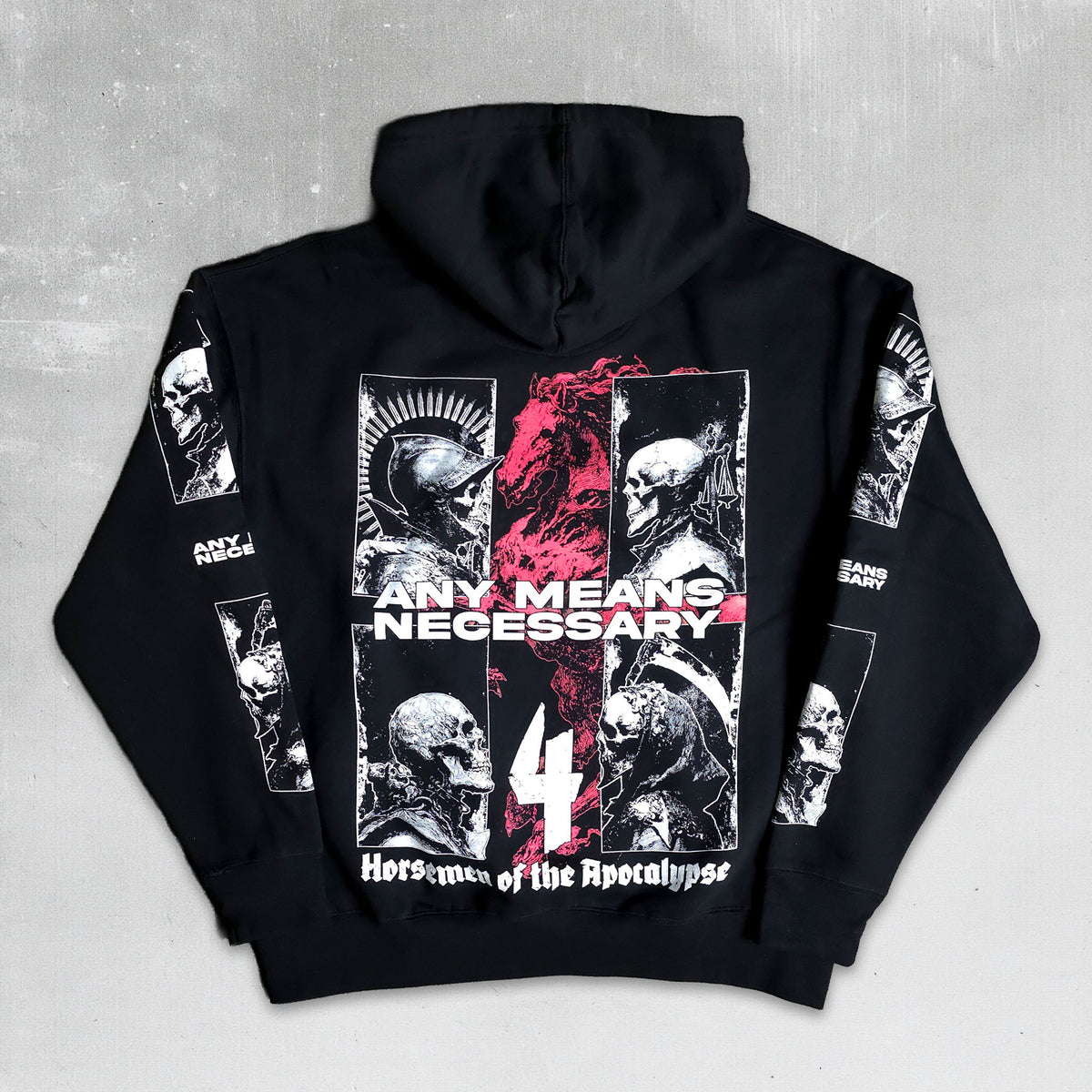 A black pullover hoodie shown flat against a textured gray background, displaying a detailed back graphic with the text 'ANY MEANS NECESSARY', a large number 4, and multiple black-and-white skull illustrations with red accents.