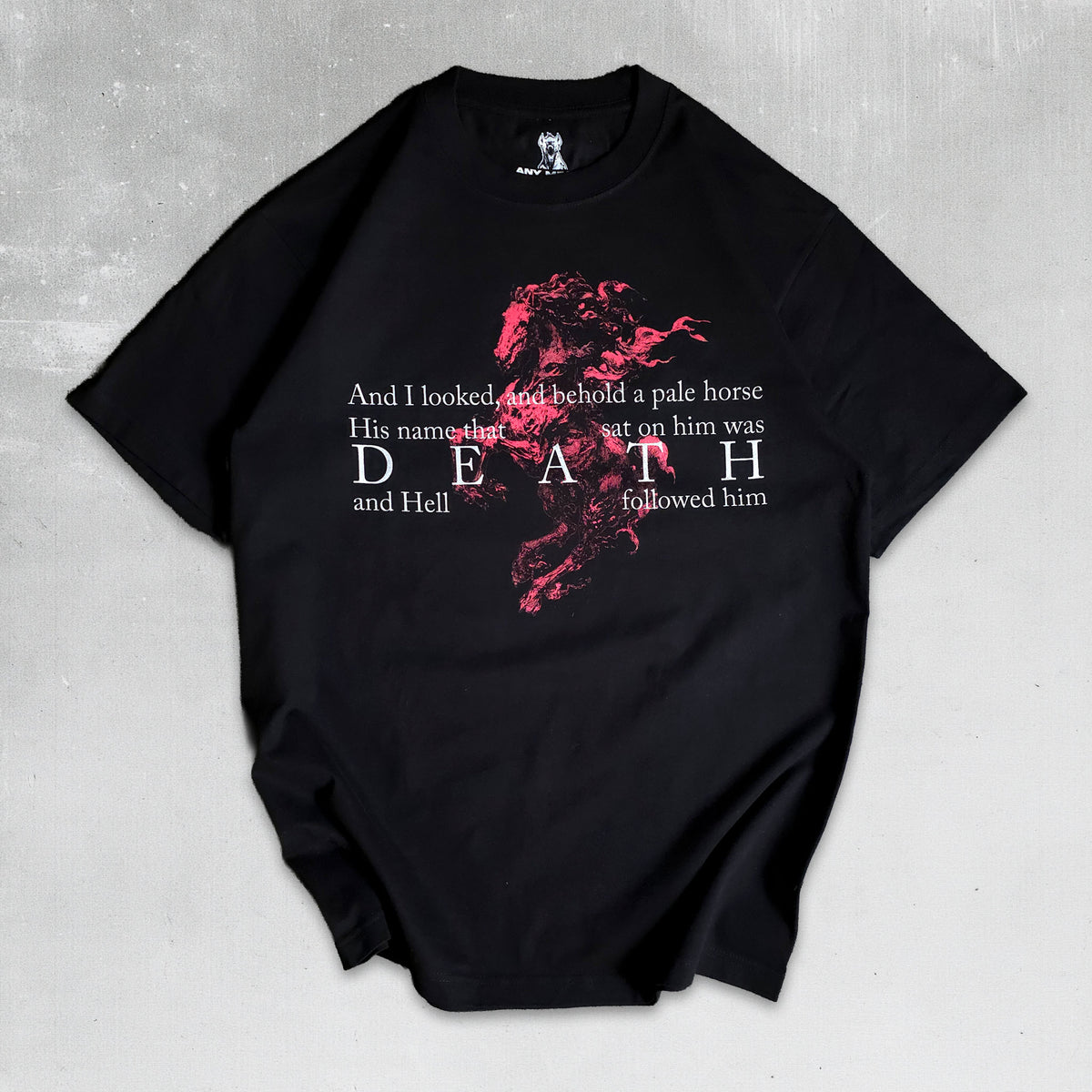 A black short-sleeve t-shirt with a graphic print of a red horse and white text, laid flat on a textured gray background.