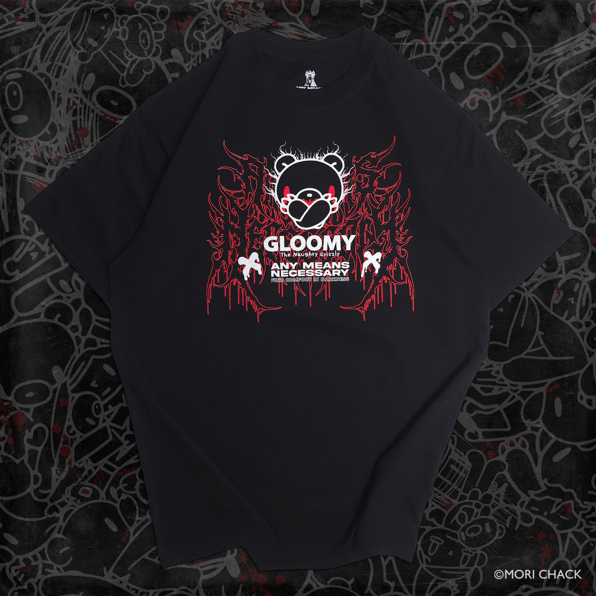 A black short-sleeve graphic t-shirt laid flat on a dark, graffiti-patterned background. The shirt features a central graphic of a gloomy, faceless character wearing a red and white mask, surrounded by red dripping ink-like details and white text that reads 'GLOOMY' and 'ANY MEANS NECESSARY'.