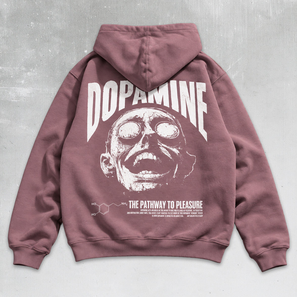 A dusty rose hoodie shown from the back, featuring a large white graphic print of a zombie face with the word 'DOPAMINE' above it and smaller text below reading 'THE PATHWAY TO PLEASURE' alongside a chemical structure diagram. The hoodie is laid flat against a textured gray background.