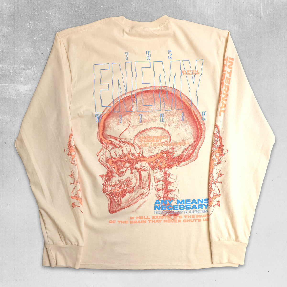 A cream-colored long-sleeve t-shirt with a large graphic print on the back, featuring a red anatomical skull and blue and orange text that reads 'THE ENEMY WITHIN' and 'ANY MEANS NECESSARY'.