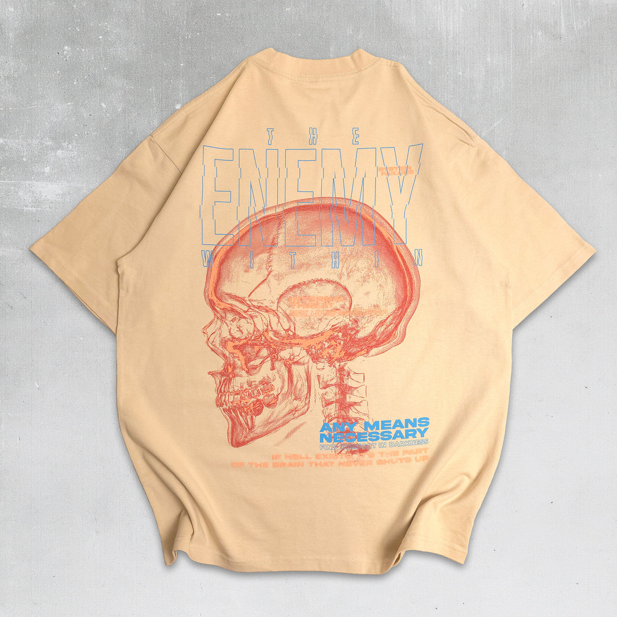 A beige oversized short-sleeve t-shirt with a large graphic print on the back, featuring a red anatomical skull and blue text that reads 'THE ENEMY WINS WIN' and 'ALL MEANS NECESSARY'.