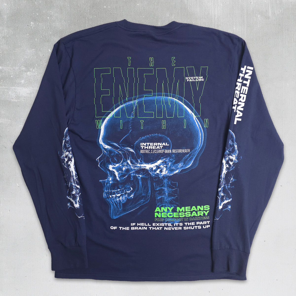 A navy blue long-sleeve t-shirt with a large graphic print on the back, featuring a glowing blue skull, green and white text, and white lightning bolt designs on the sleeves, laid flat on a gray concrete background.