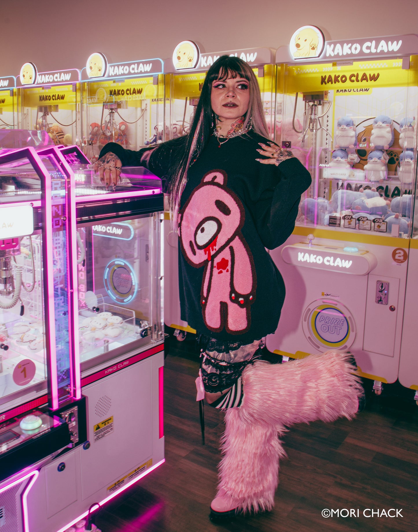 Person in a black hoodie with a pink bear design in front of claw machines.