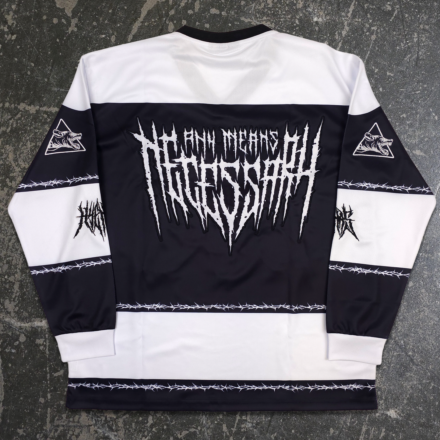 A long-sleeve black and white hockey-style jersey laid flat on a dark textured surface, featuring a large white spiky logo across the chest reading 'Death Means Progress' and additional black logo graphics on the sleeves and lower hem. any means necessary shawn coss goon squad hockey jersey