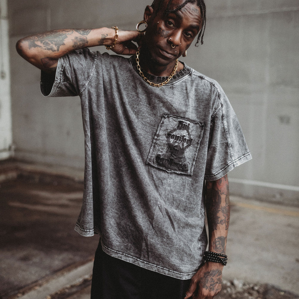 
                      
                        Person wearing a gray t-shirt with a graphic design, standing in an abandoned building.
                      
                    