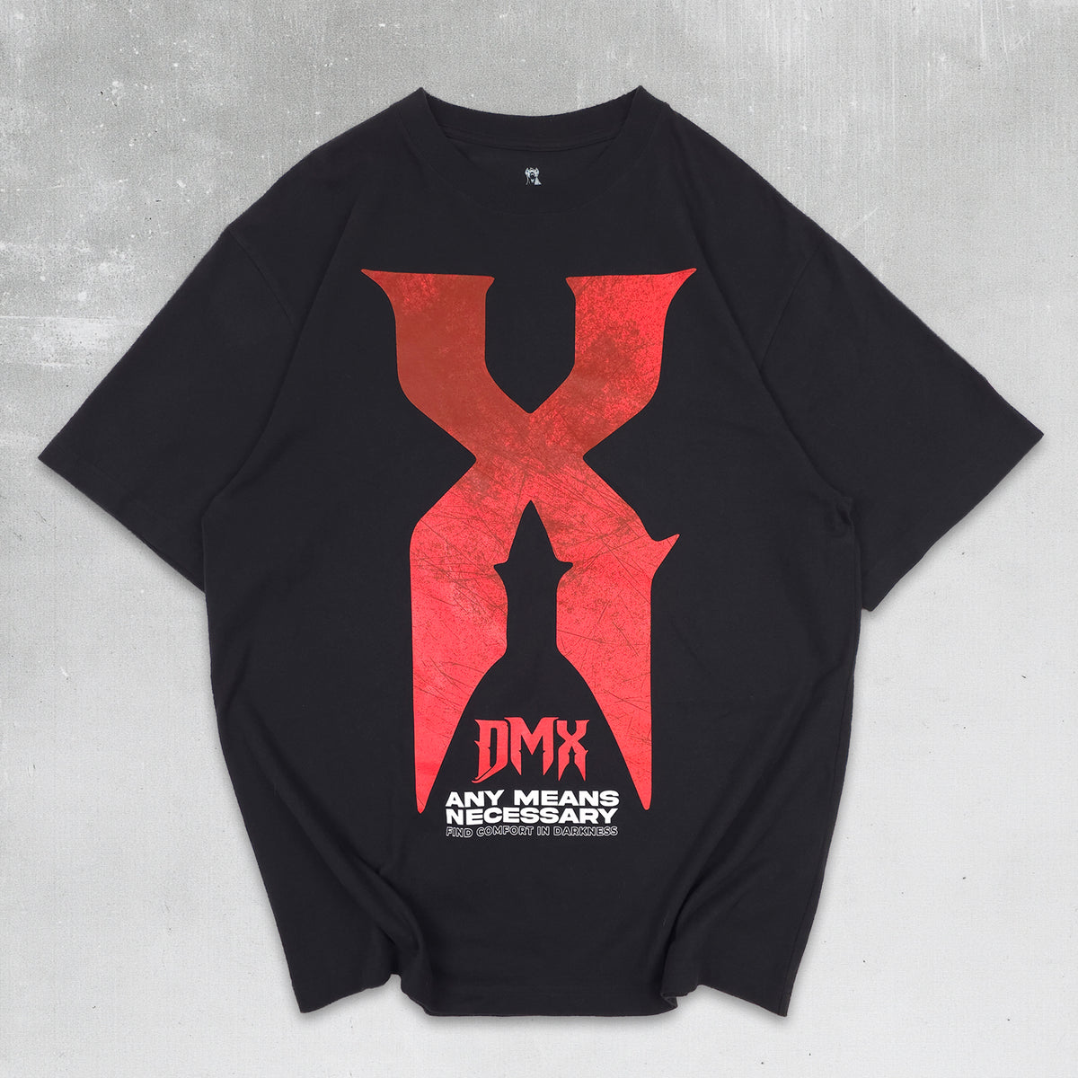 A black short-sleeve t-shirt with a large red distressed 'X' graphic on the front, featuring a black silhouette in the center and the text 'DMX ANY MEANS NECESSARY' printed below it. The t-shirt is laid flat on a textured gray background.