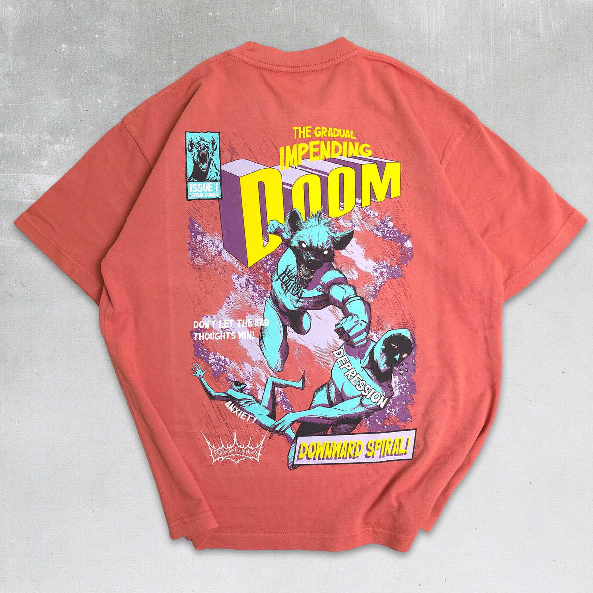 A coral red graphic t-shirt laid flat on a textured gray background, featuring a large comic-style print with the word 'DOOM' and illustrated characters.