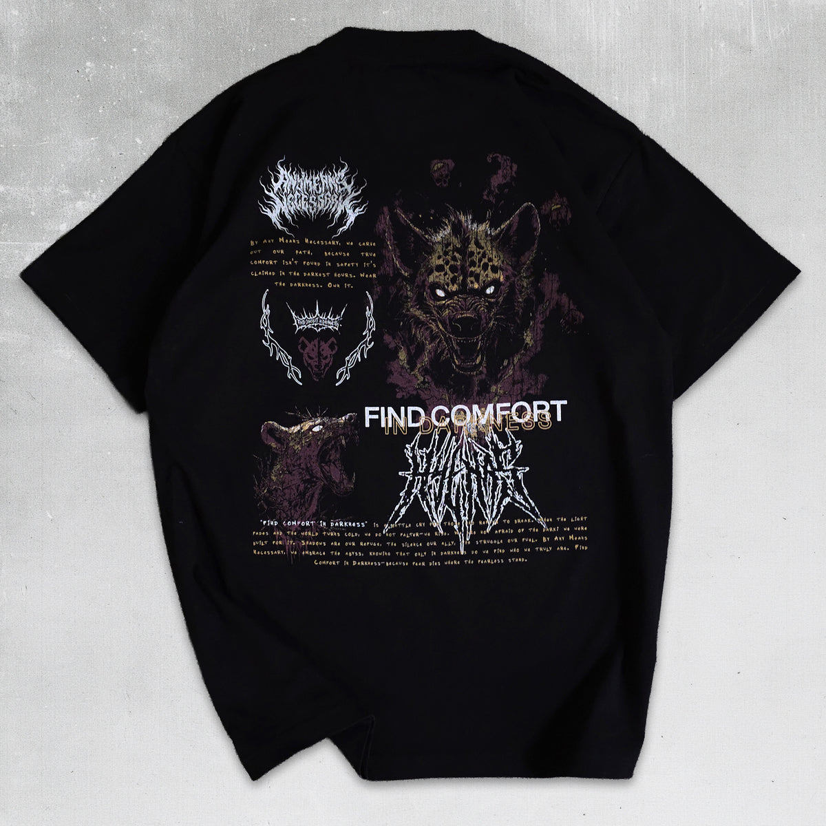 A black short-sleeve graphic t-shirt laid flat on a textured gray background, featuring a detailed dark gothic and metal-themed print with a hyena, a horned skull, and the text 'FIND COMFORT' and 'THE CROWN IS LONELY'.