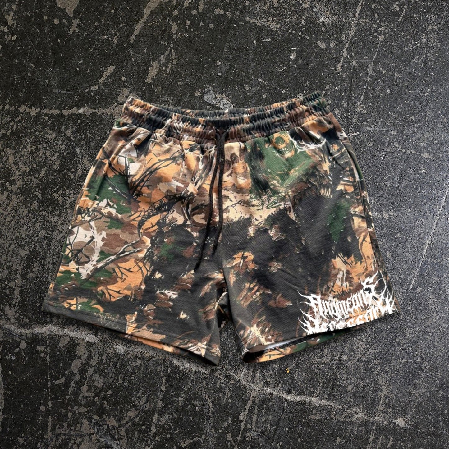 Camouflage shorts on a textured black surface any means necessary shawn coss find comfort in darkness rogue woods mayhem shorts camo front