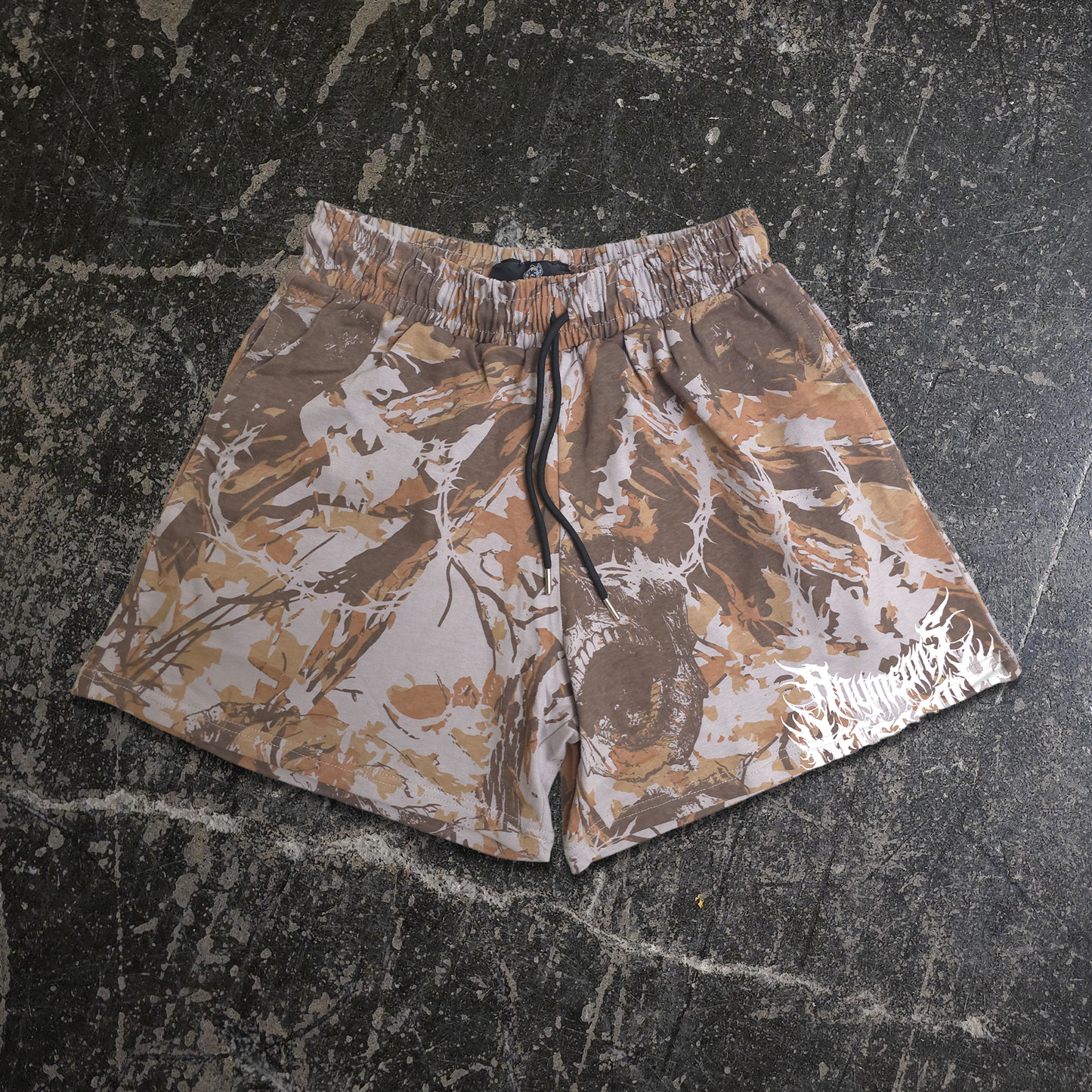 Camouflage shorts on a textured black surface any means necessary shawn coss find comfort in darkness deadwood mayhem shorts camo front