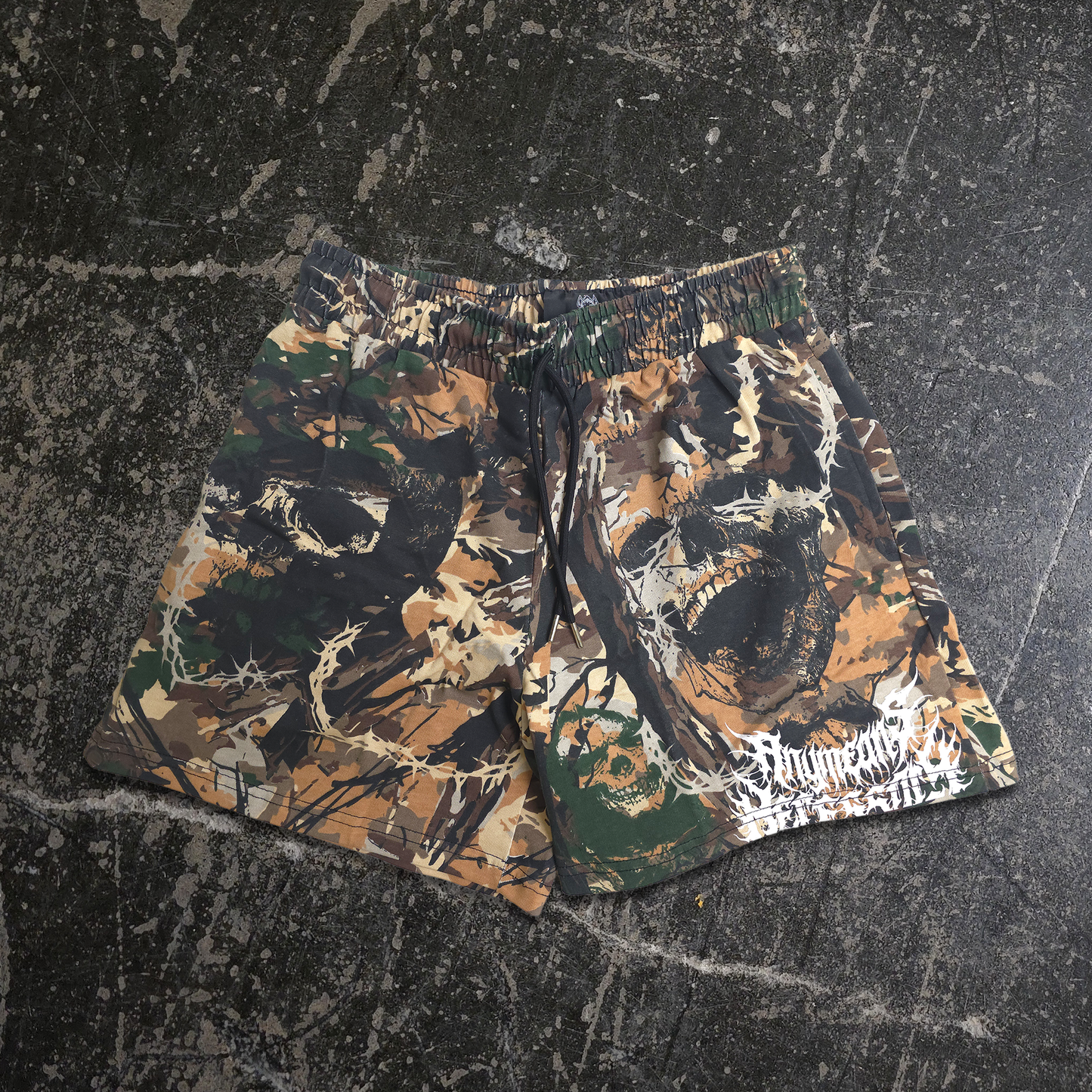 Camouflage shorts on a textured black surface any means necessary shawn coss find comfort in darkness rogue woods mayhem shorts camo front