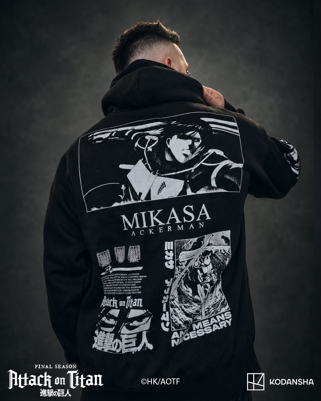 A man shown from the back wearing a black hoodie with a large white Attack on Titan Mikasa Ackerman graphic print on the back, set against a dark textured studio background.