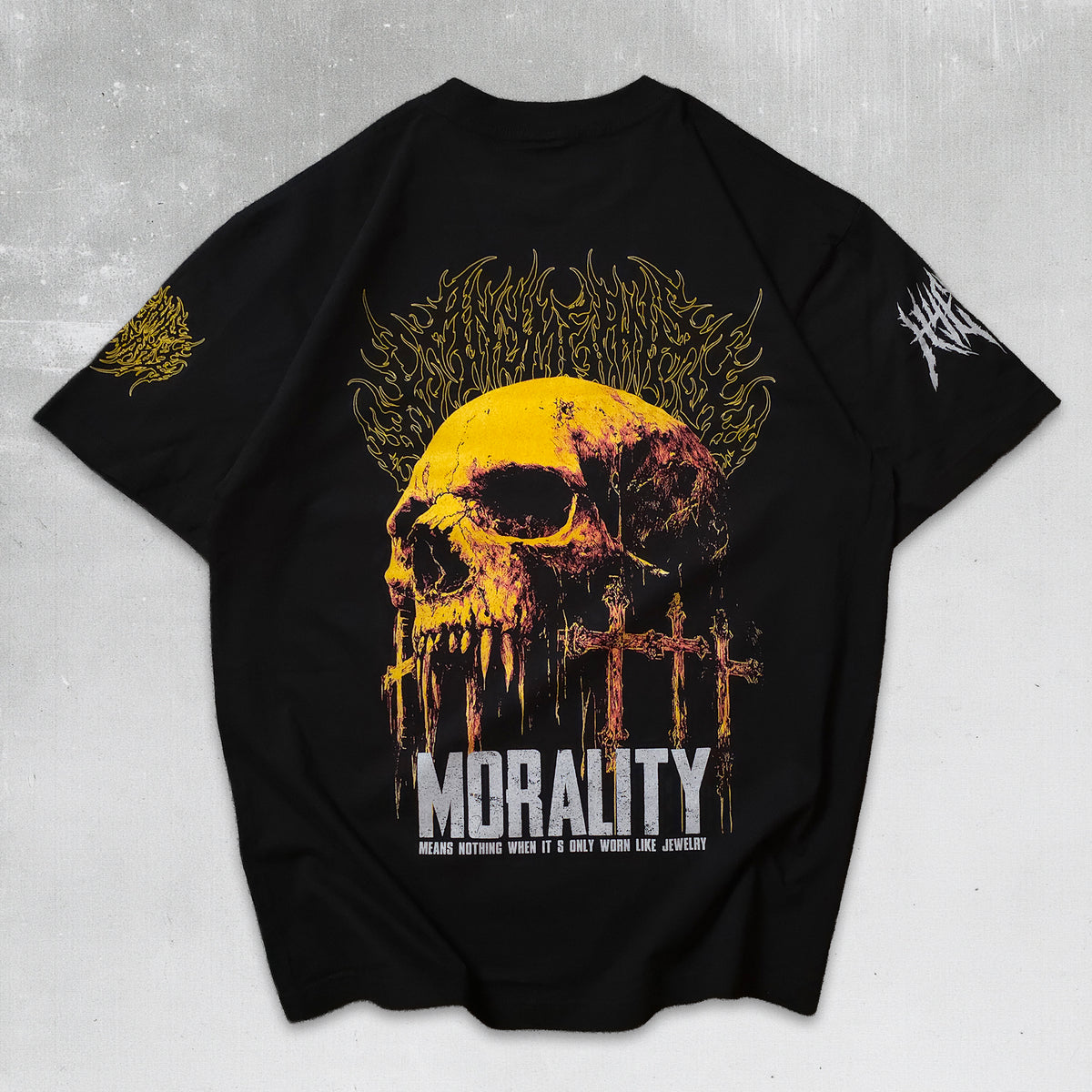 A black short-sleeve graphic t-shirt featuring a large yellow and orange skull design with the word 'MORALITY' in white distressed text below it, displayed flat against a textured gray background.