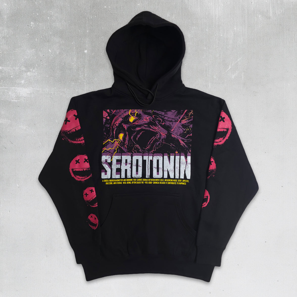 A black pullover hoodie with a large graphic print on the chest and pink smiley-face designs on both sleeves, laid flat against a textured gray background.