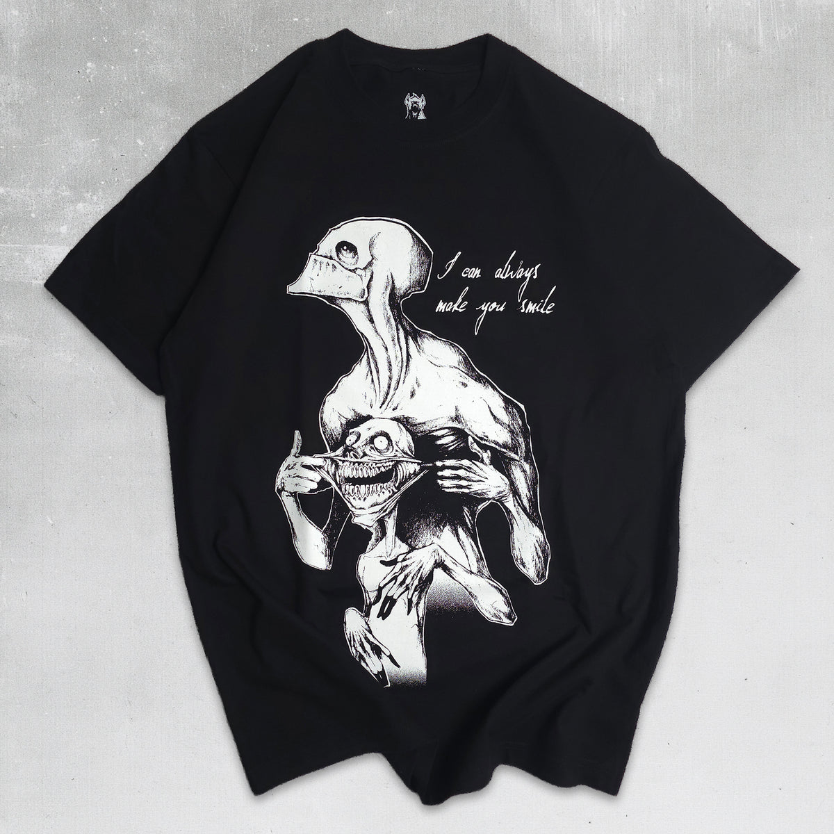 A black oversized short-sleeve t-shirt with a detailed white graphic print of a skeletal figure holding a skull, accompanied by the handwritten text 'I can always make you smile' on a textured gray background.